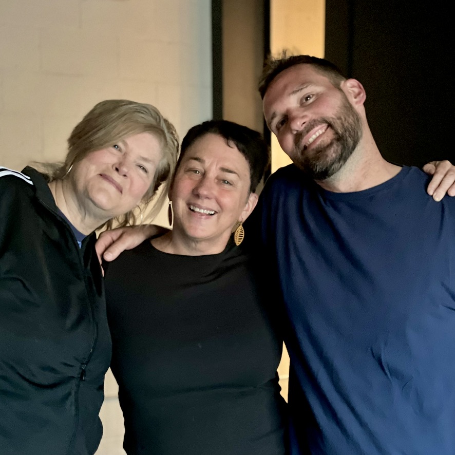 Three performers smiling together backstage