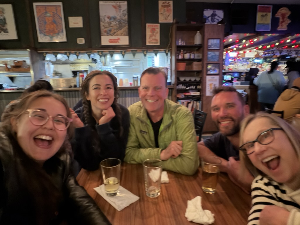 Cast members laughing around a table at the pub